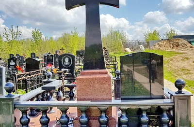 Простой крест на тумбе слева от невысокого надгробья